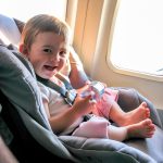happy toddler flying in a car seat on airplane
